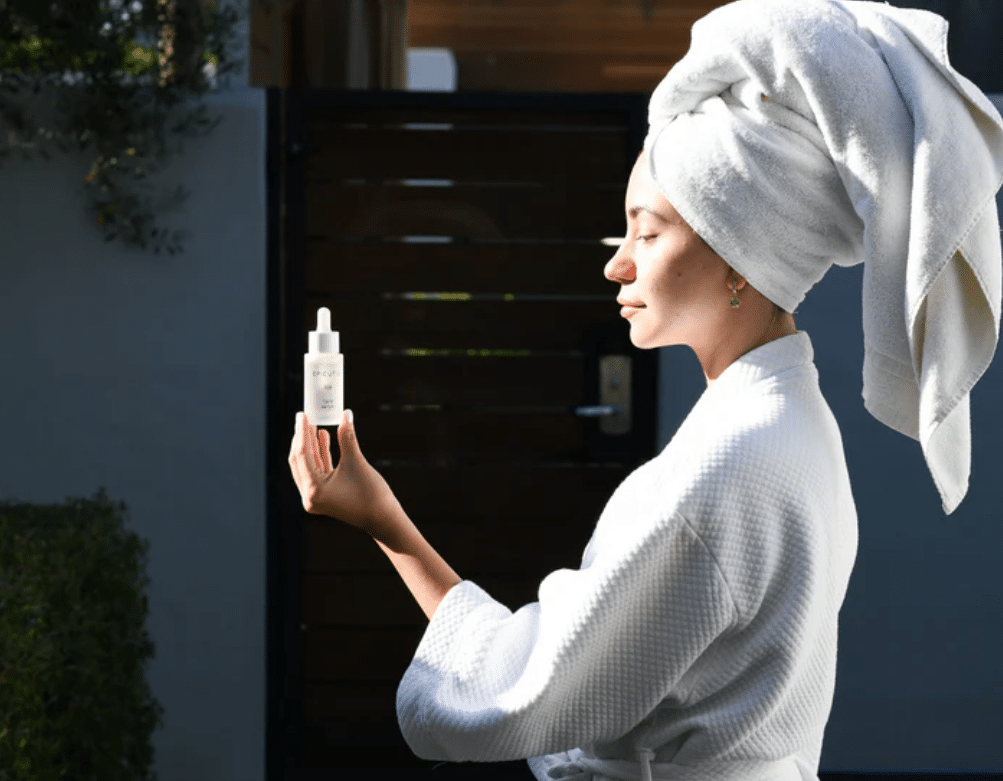 Woman in spa robe holding Epicutis Skincare serum in natural sunlight, showcasing a clean and minimal skincare routine.